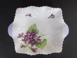 On the top of this dish has violets in various states of bloom and foliage scattered on the dish. This trinket dish is...
