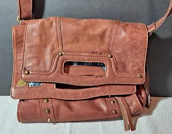 Made of distressed brown leather, it features a foldover design with studded accents, an adjustable shoulder strap, and...