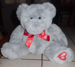 HE IS LIGHT GREY WITH A RED RIBBON THAT HAS SHINY HEARTS AND HE HAS AN XO PATCH ON HIS LEFT FOOT. SEE PHOTOS.