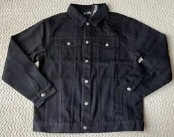 The jacket is a classic denim trucker jacket in black denim. It buttons down the front and has side pockets, flap...