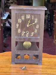 Antique Mission Oak Clock having brass numbered dial and and brass hands on the face. Key and pendulum present. The...