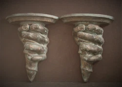 Crafted in 1994, this set of two pottery wall shelves features hands grasping the shaft of a torch; signed on back....