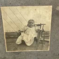 This is a antique photo of a baby sitting on a wicker stroller. Photo has some discoloration from age. Nice...