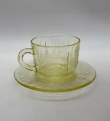 Light yellow depression glass cup and saucer with floral design.