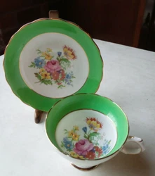 Light green trim on cup and saucer, with scalloped edges and colorful flower bouquet of roses, daisies, blue, red, pink...