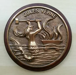 Plaque en bronze fixée sur bois. Diamètre bronze : 12 cm. Diamètre bois : 13,9 cm.