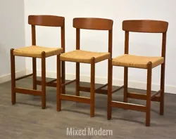 A set of three mid century modern teak bar stools with paper cord seats. Seat height is 24”.