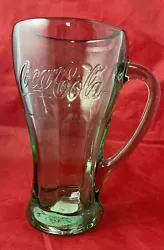 It features a green color and a handle for easy grip. The mug is adorned with the iconic Coca-Cola logo and is a great...