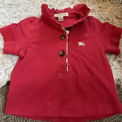 Elevate your little girls style with this beautiful red Burberry polo shirt. Made from 100% cotton material, this...