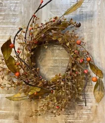 This is a new wreath that has artificial orange berries, brown twigs and green leaves on a flexible brown vine.