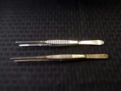 Lot of 2 tweezers. Good used condition. Has wear and discoloration. One is missing the interior bar. Flat rounded grip...