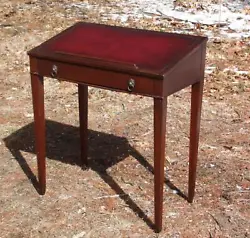 Features slanted top with tooled red leather and pencil holder, a dovetailed drawer with brass lion ring pulls and...