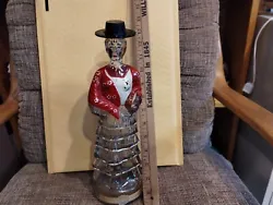 This antique figural bottle stands at 13 inches tall and features a dancer wearing a hat. The bottle is clear in color...