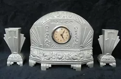 Superbe pendule ou horloge en métal Art Déco avec sa paire de cassolettes ou vases. Des années 20s 30s. Elle est...