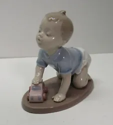 Lladro small child/baby in blue shirt, wearing a diaper, pushing a pink car. Approx 4-3/4