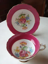 Dark red trim on cup and saucer, with scalloped edges and colorful flower bouquet of roses, daisies, blue, red, pink...